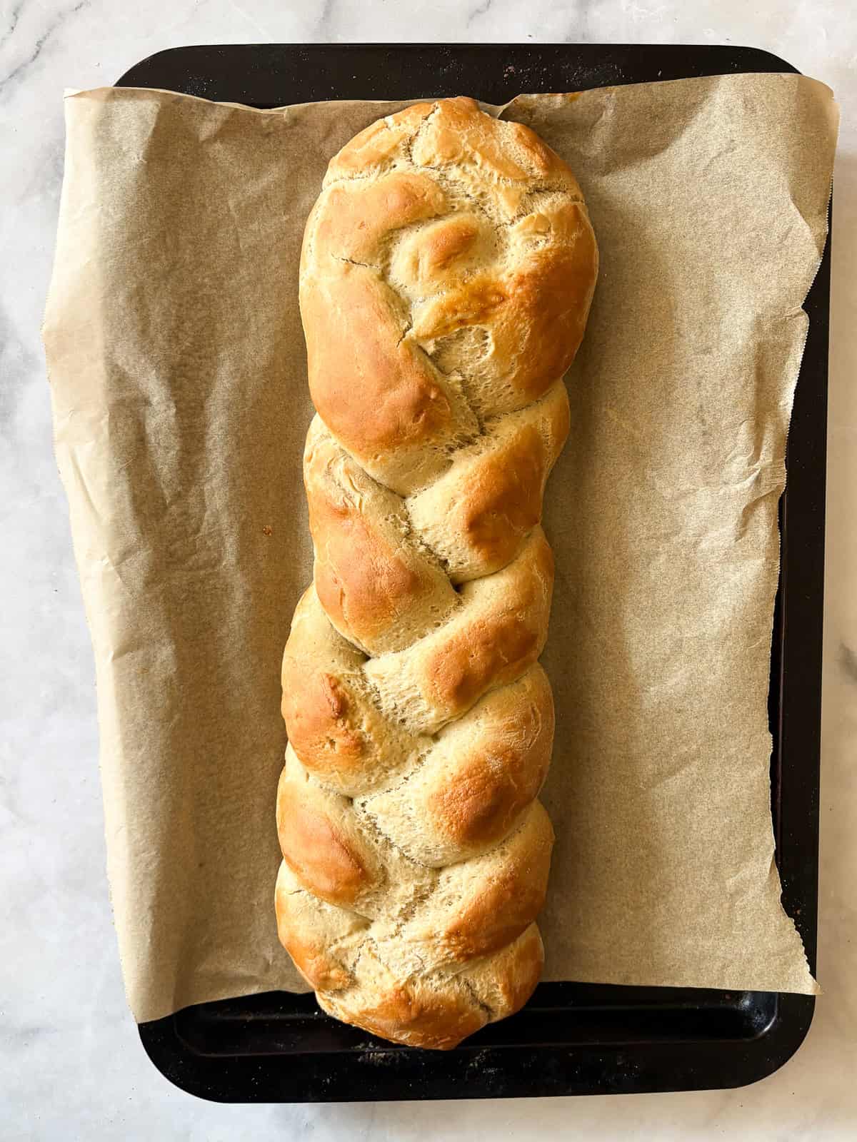 A gum-free recipe for a beautifully soft loaf of gluten free challah that's easy enough even for novice gluten-free bread bakers. A gluten free challah after being baked on a baking sheet.