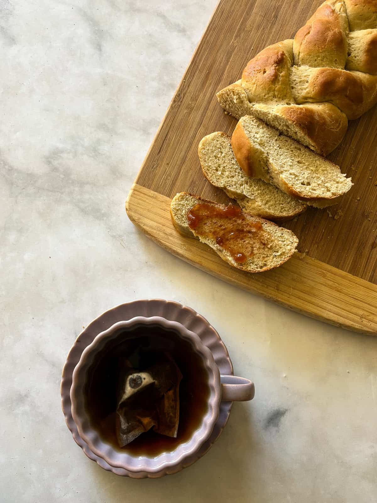 A gum-free recipe for a beautifully soft loaf of gluten free challah that's easy enough even for novice gluten-free bread bakers. A cup of tea next to a sliced loaf of gluten free challah.