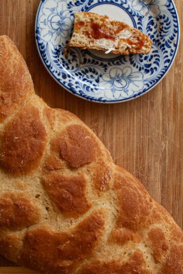 A golden braided loaf of gluten free challah and a slice of challah on a plate.