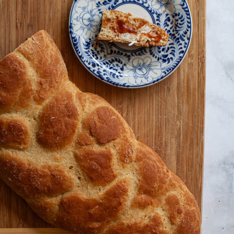 A golden braided loaf of gluten free challah and a slice of challah on a plate.