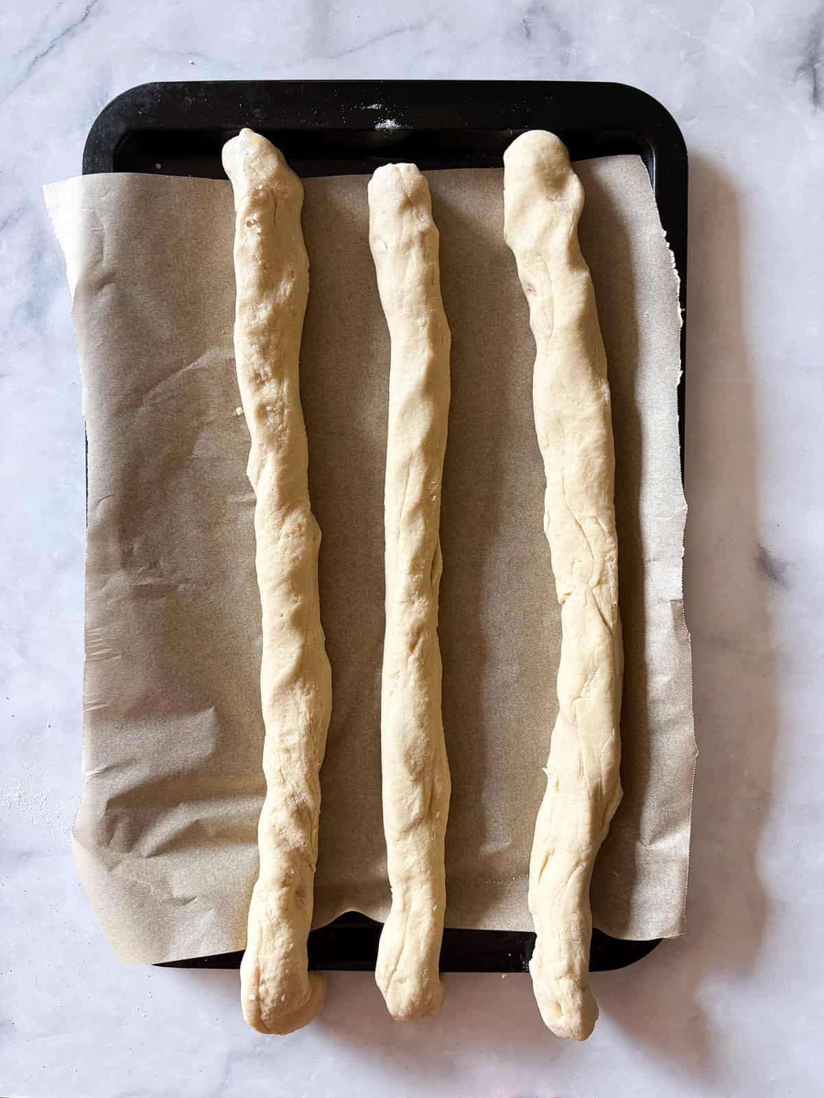 A gum-free recipe for a beautifully soft loaf of gluten free challah that's easy enough even for novice gluten-free bread bakers. Gluten free challah dough formed into three logs.