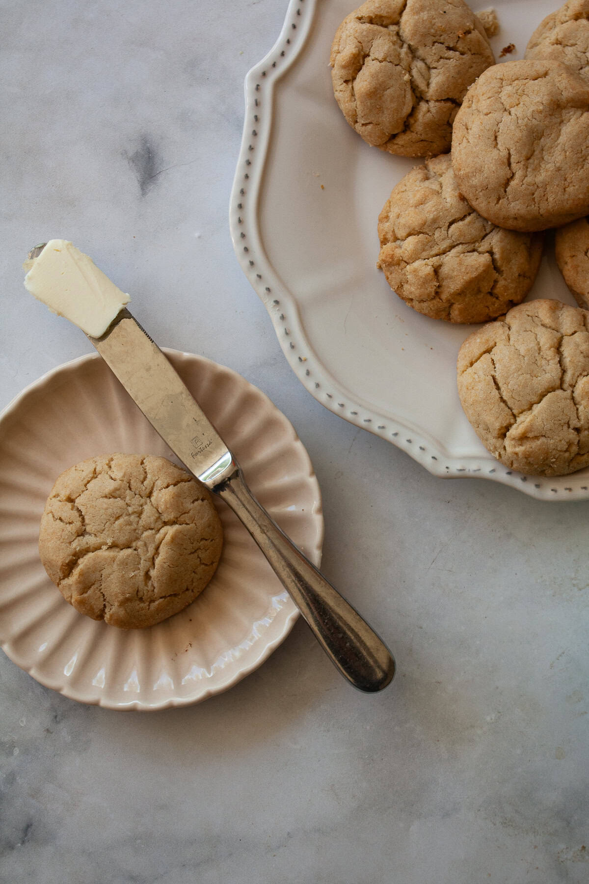 A gluten free cream biscuit on a plate with a knife next to the plate of biscuits.