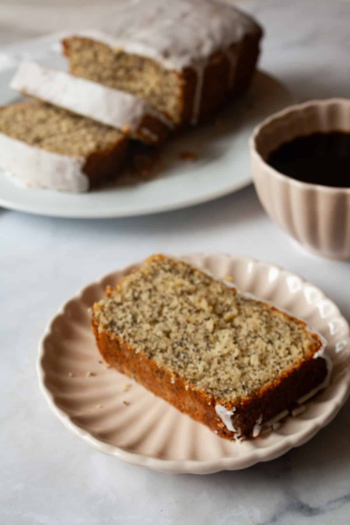 A tender, gorgeously sliceable gluten free lemon poppyseed bread topped with a bright, thick lemon glaze for maximum flavor. Gluten free lemon poppyseed bread on a plate with a cup of coffee.