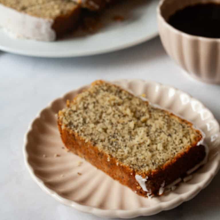 Gluten free lemon poppyseed bread on a plate with a cup of coffee.