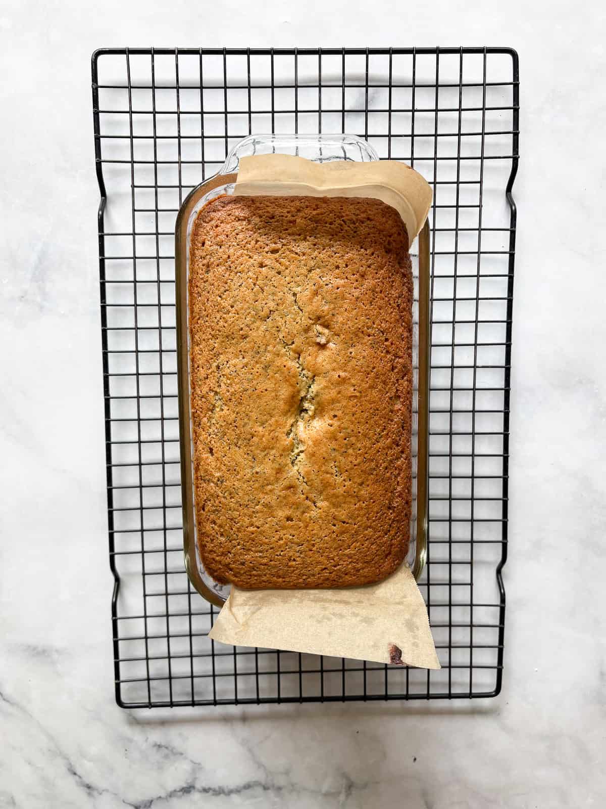 A tender, gorgeously sliceable gluten free lemon poppyseed bread topped with a bright, thick lemon glaze for maximum flavor. A baked loaf of gluten free lemon poppyseed bread cools on a rack.
