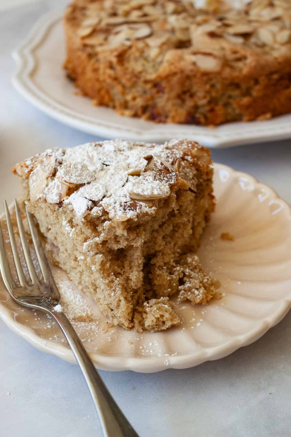 Powdered sugar tops a slice of gluten free rhubarb cake on a plate with a fork.