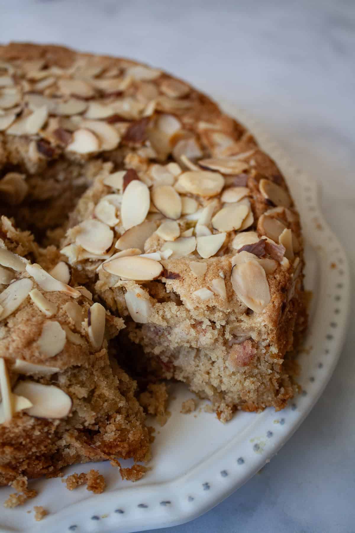 Tart rhubarb is the star of this gluten free rhubarb cake, with jammy pockets of rhubarb and a soft-crumbed cake that's just sweet enough. A piece of gluten free rhubarb cake is removed from the cake.