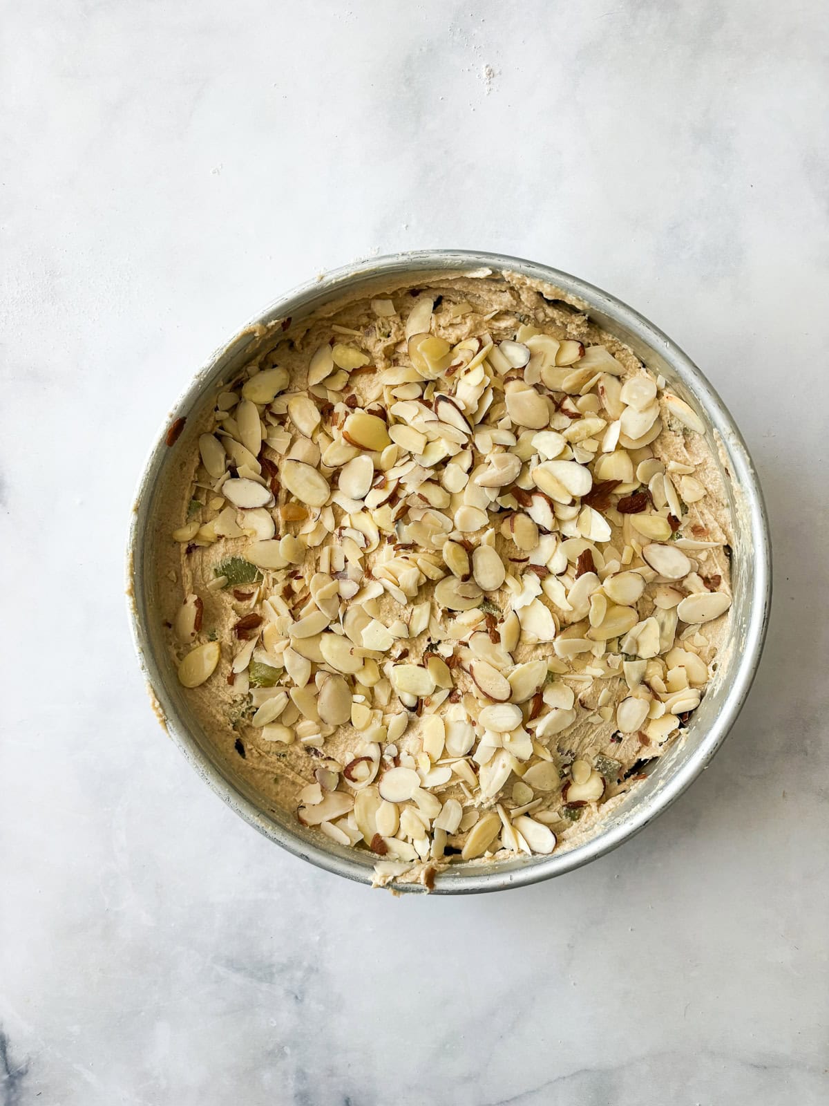 Tart rhubarb is the star of this gluten free rhubarb cake, with jammy pockets of rhubarb and a soft-crumbed cake that's just sweet enough. Almonds are scattered over the top of gluten free rhubarb cake batter in a pan.