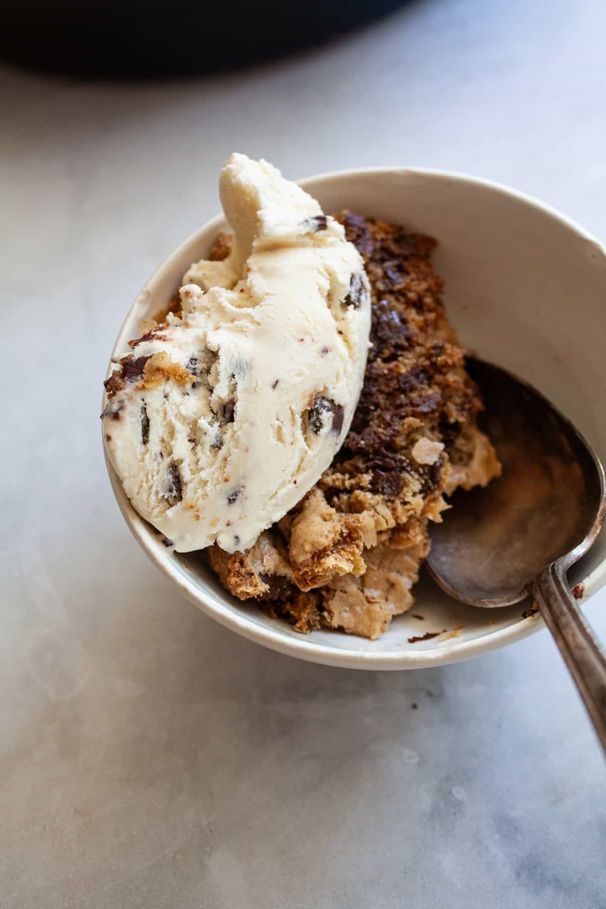 This sweet and chewy gluten free skillet cookie that's soooo good served warm and topped with ice cream. Made in one bowl! A serving of gluten free skillet cookie in a bowl topped with ice cream.