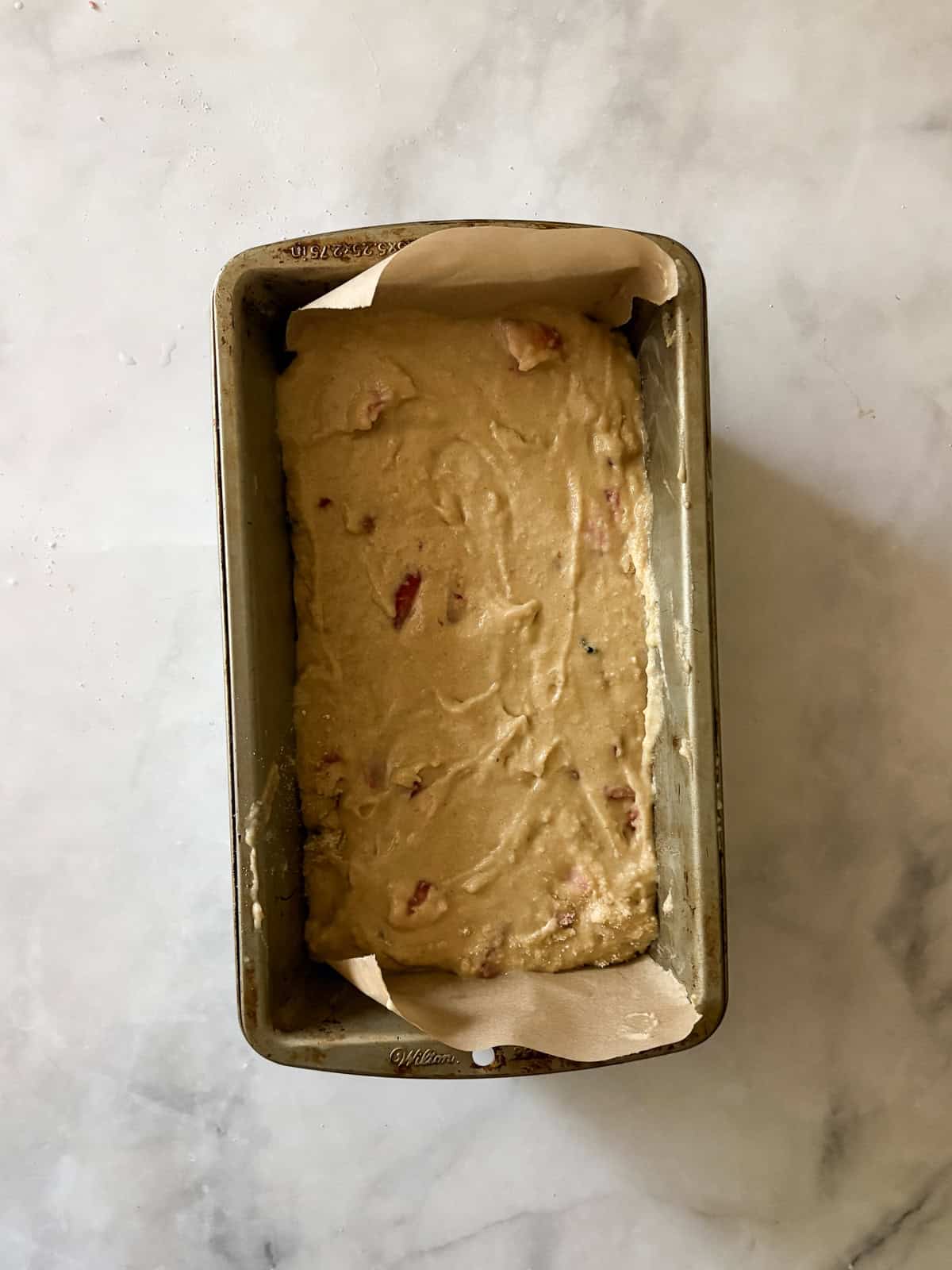 A tender, fruit-flecked gluten-free strawberry loaf cake topped with a simple and sweet vanilla glaze. The best summery bake! A loaf pan is filled with gluten strawberry loaf cake batter.
