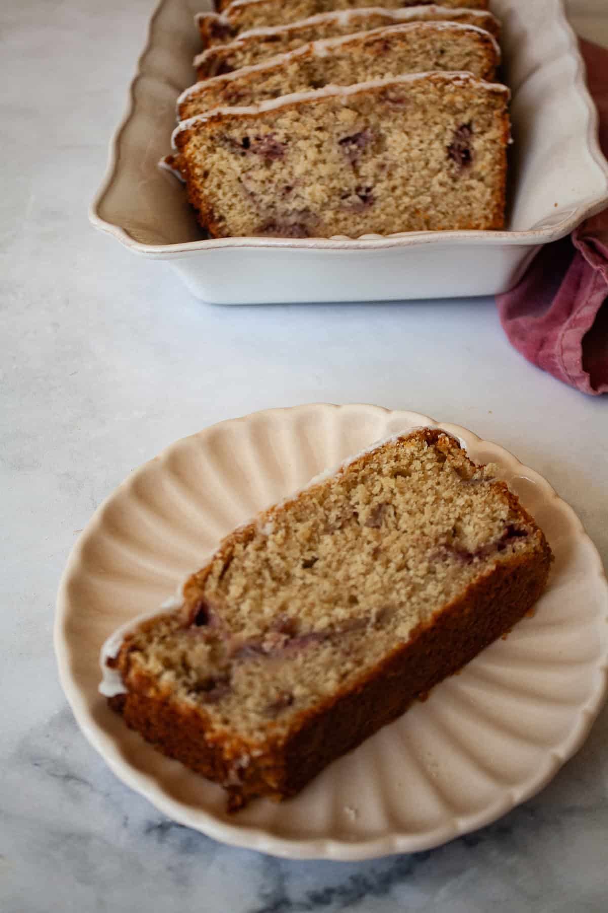 A tender, fruit-flecked gluten-free strawberry loaf cake topped with a simple and sweet vanilla glaze. The best summery bake! A slice of gluten free strawberry loaf cake on a plate.