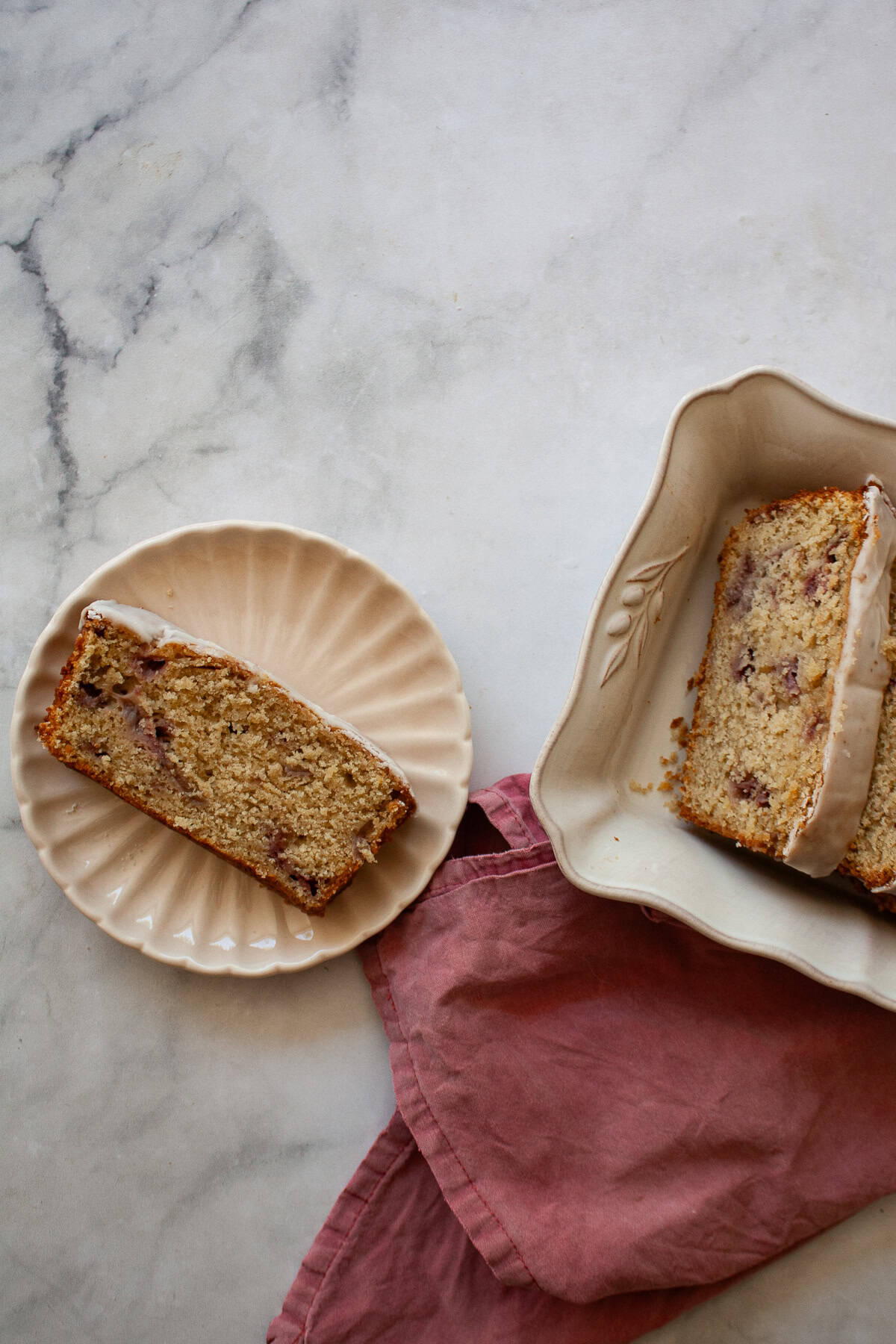A tender, fruit-flecked gluten-free strawberry loaf cake topped with a simple and sweet vanilla glaze. The best summery bake! A slice of gluten free strawberry loaf cake on a plate next to the cake and a red napkin.