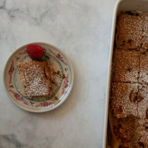 A slice of gluten free strawberry rhubarb cake on a plate next to the cake.