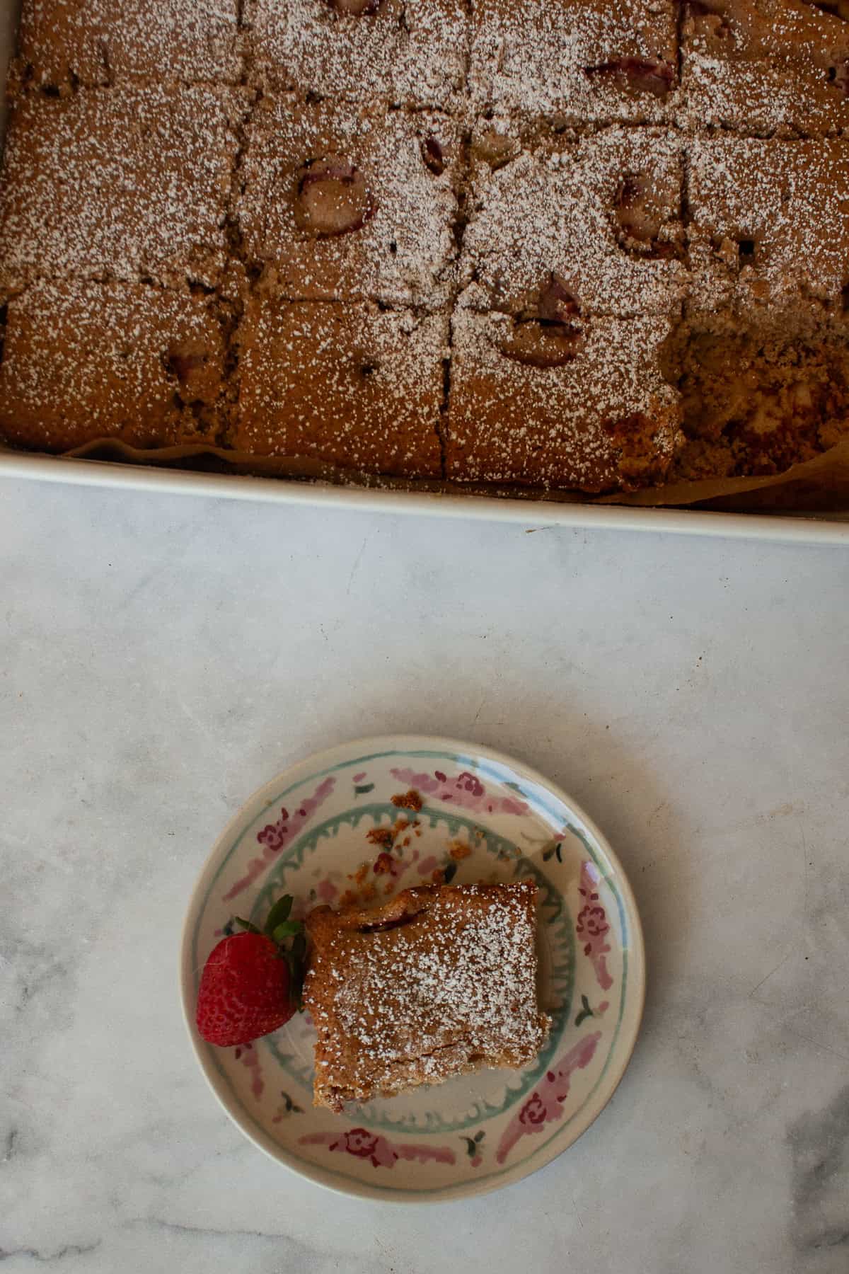A soft, buttery gluten-free strawberry rhubarb cake packed with fresh fruit. Fork-tender, easy to make, and perfect for summer dessert. A slice of gluten free strawberry rhubarb cake on a plate next to the cake.