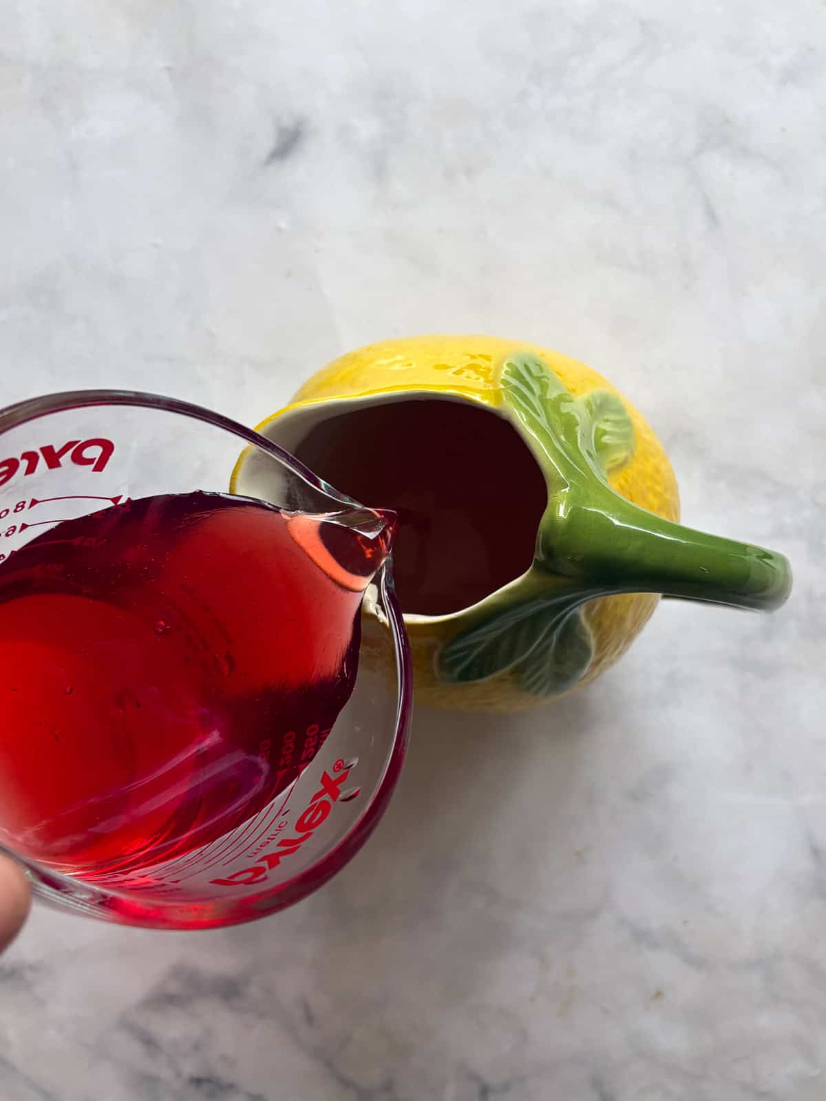 Sweet strawberry simple syrup is stirred into fresh lemon juice for a sweet-tart pitcher of homemade strawberry lemonade. Pouring strawberry simple syrup into lemon juice for strawberry lemonade.