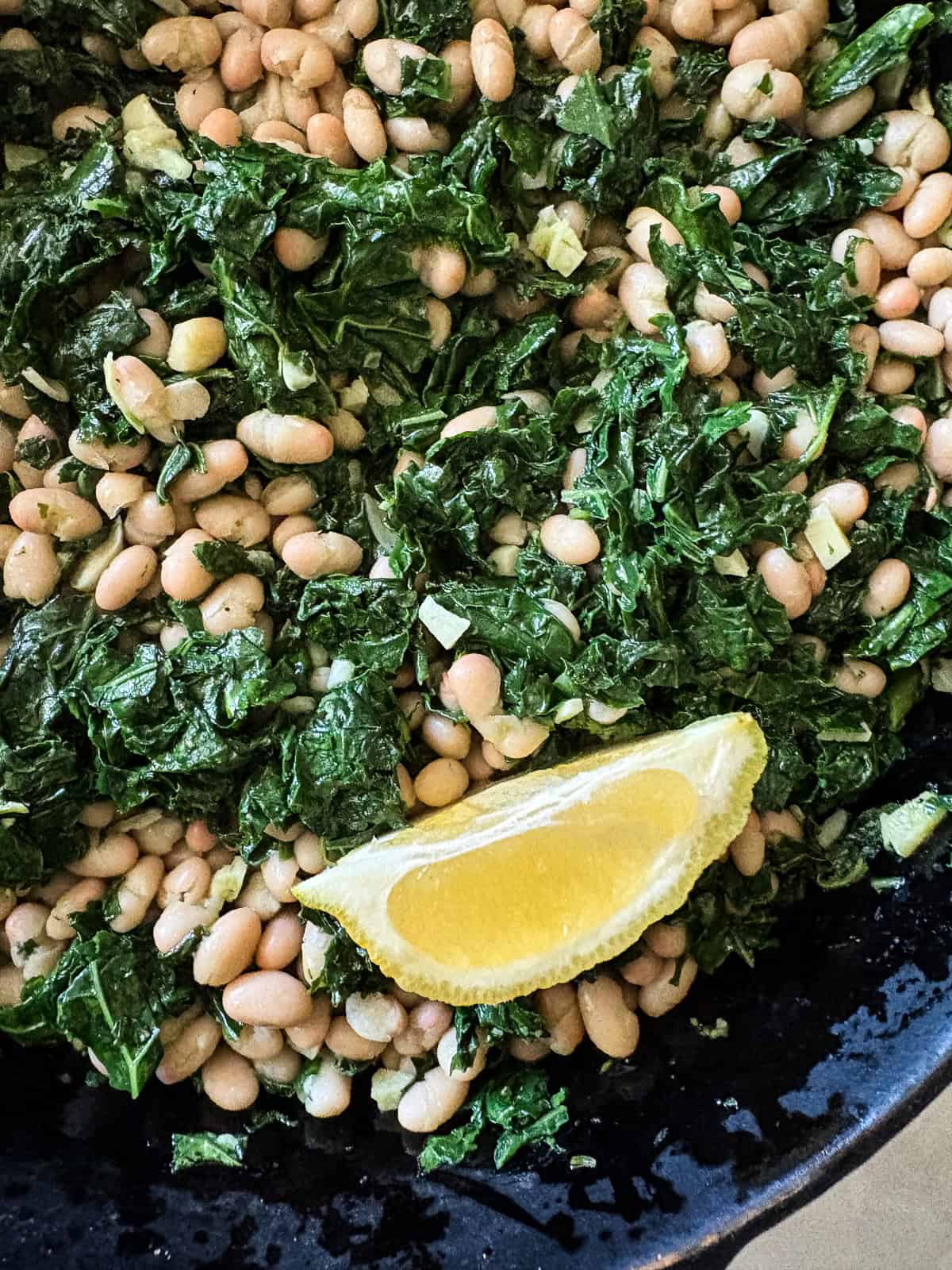 Garlicky white beans and kale are brightened up with lemon juice for a simple, satisfying, and QUICK vegetarian main. Close up of white beans and kale topped with a lemon wedge.