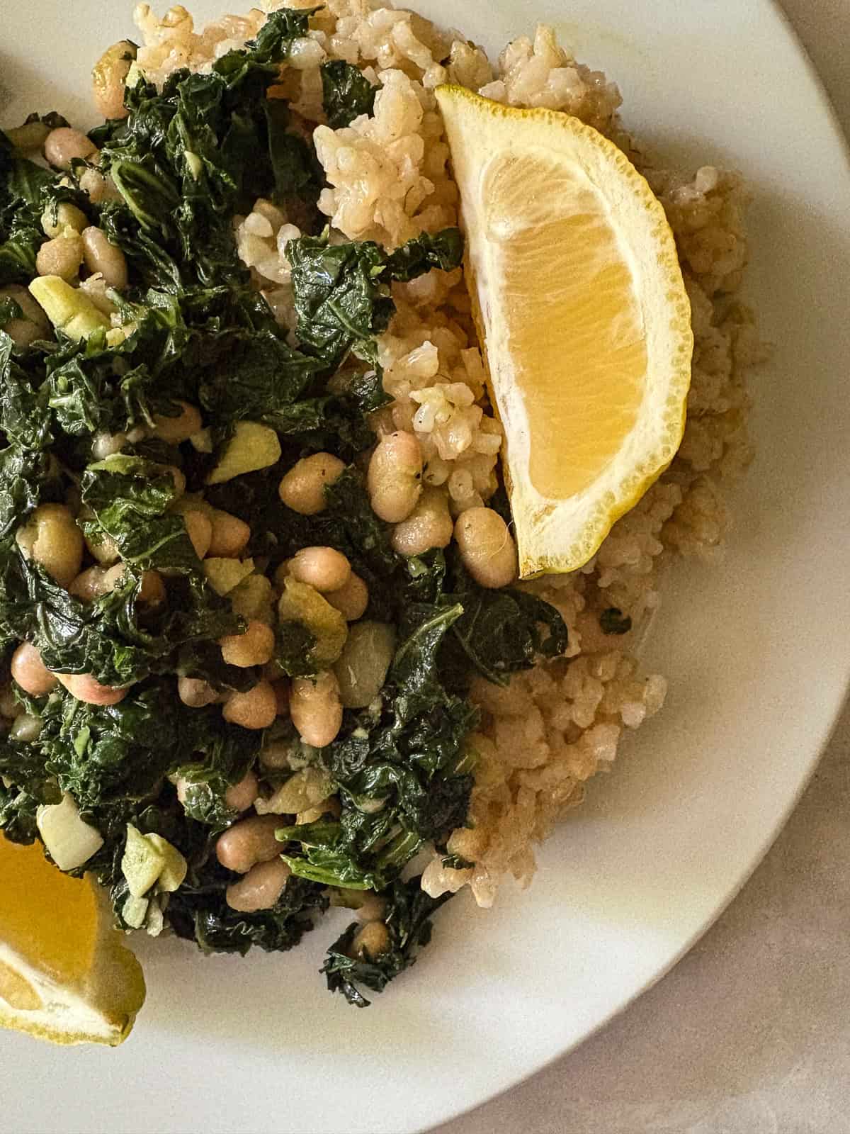 Garlicky white beans and kale are brightened up with lemon juice for a simple, satisfying, and QUICK vegetarian main. A portion of white beans and kale on a plate is topped with a lemon wedge.