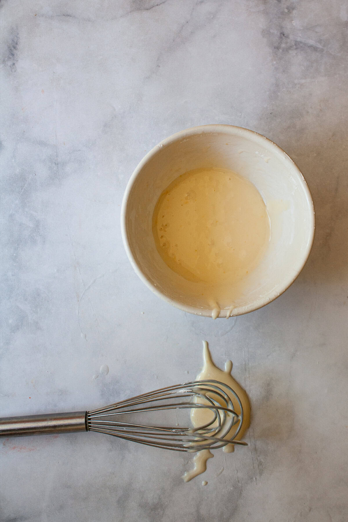 This two-ingredient orange glaze adds sweet citrus flavor to cakes, quick breads, scones, muffins, and more! A whisk lays flat next to a bowl of orange glaze.