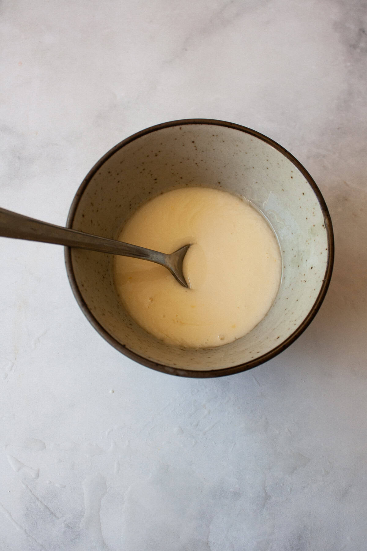 This two-ingredient orange glaze adds sweet citrus flavor to cakes, quick breads, scones, muffins, and more! A spoon rests in a bowl of orange glaze.