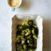 A serving dish filled with parmesan roasted broccoli and a little dish of cheese.