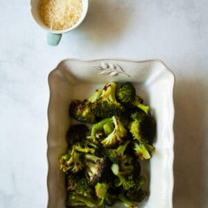 A serving dish filled with parmesan roasted broccoli and a little dish of cheese.