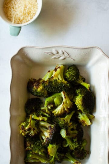 A serving dish filled with parmesan roasted broccoli and a little dish of cheese.