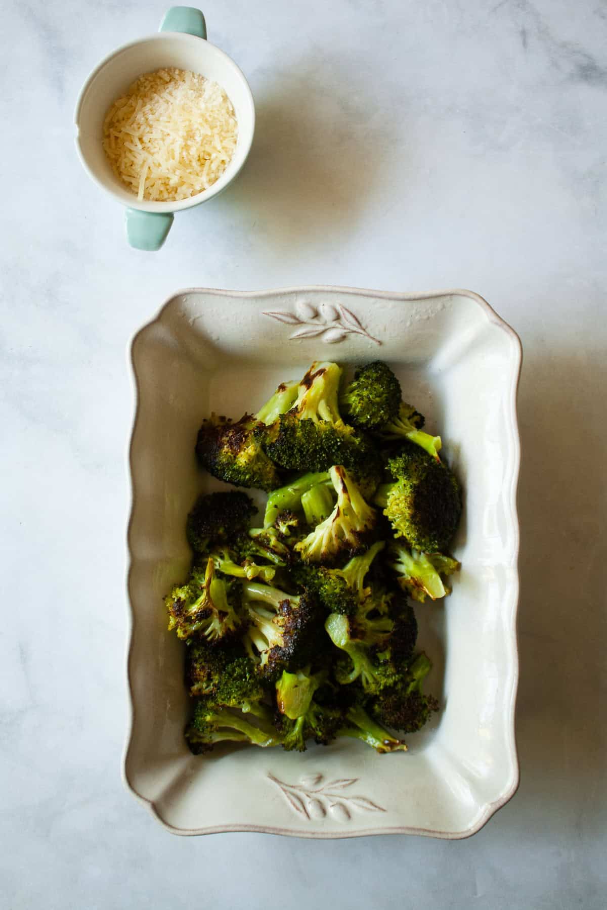 An easy recipe for roasted broccoli that can be boosted with lemon juice or zest, garlic, red pepper flakes - or simply dusted with Parmesan. A serving dish filled with parmesan roasted broccoli and a little dish of cheese.