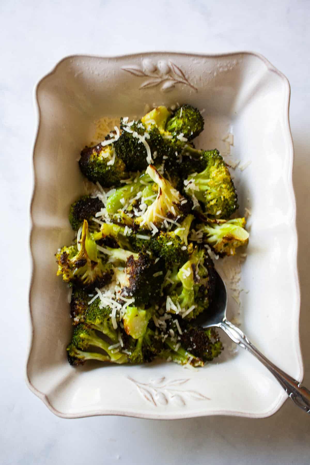 An easy recipe for roasted broccoli that can be boosted with lemon juice or zest, garlic, red pepper flakes - or simply dusted with Parmesan. A serving spoon in a serving dish of parmesan roasted broccoli.