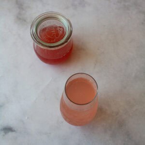 A rhubarb cocktail in front of a jar of rhubarb simple syrup.