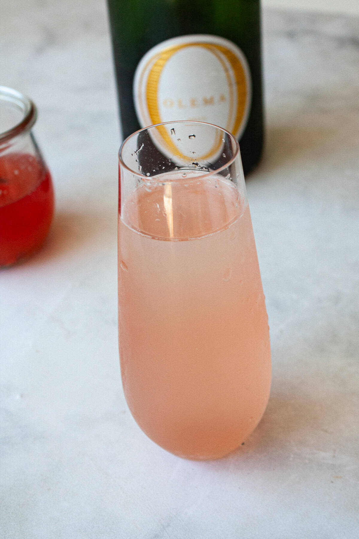 A glass of rhubarb cocktail in front of a bottle of wine.