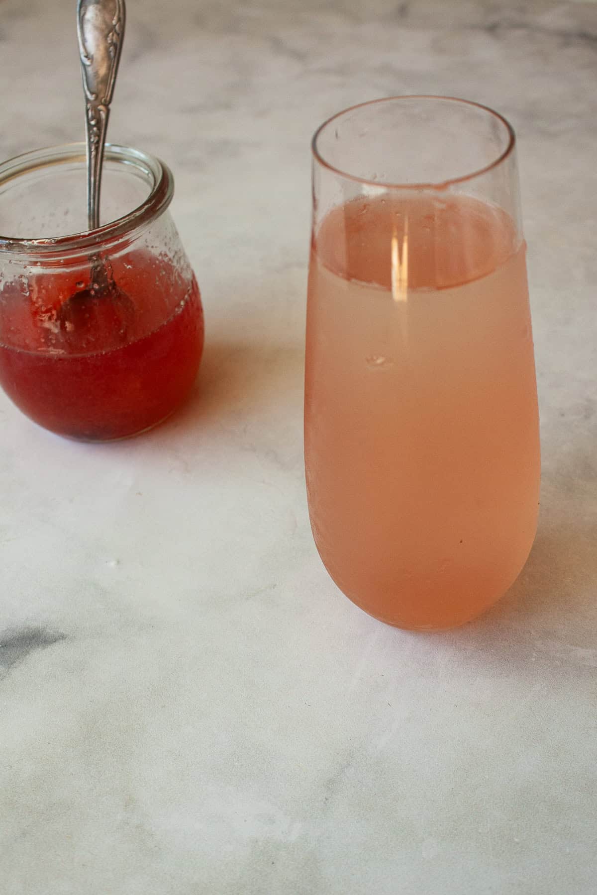 Bubbly, pink, and perfect for spring, this 2-ingredient rhubarb cocktail is sure to be your new favorite drink. A glass of rhubarb cocktail next to a jar of rhubarb simple syrup.