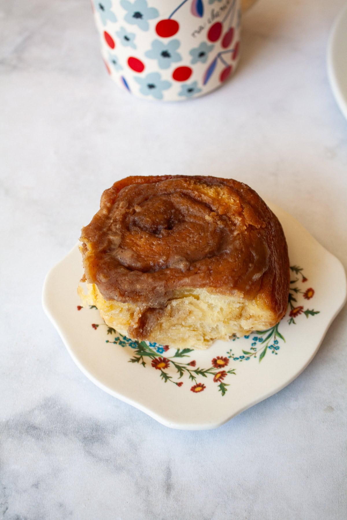 My homemade sticky buns recipe is make-ahead friendly and amazingly good! A thick maple syrup topping turns these into a bakery-worthy treat. A maple glaze sticky bun on a pretty plate.