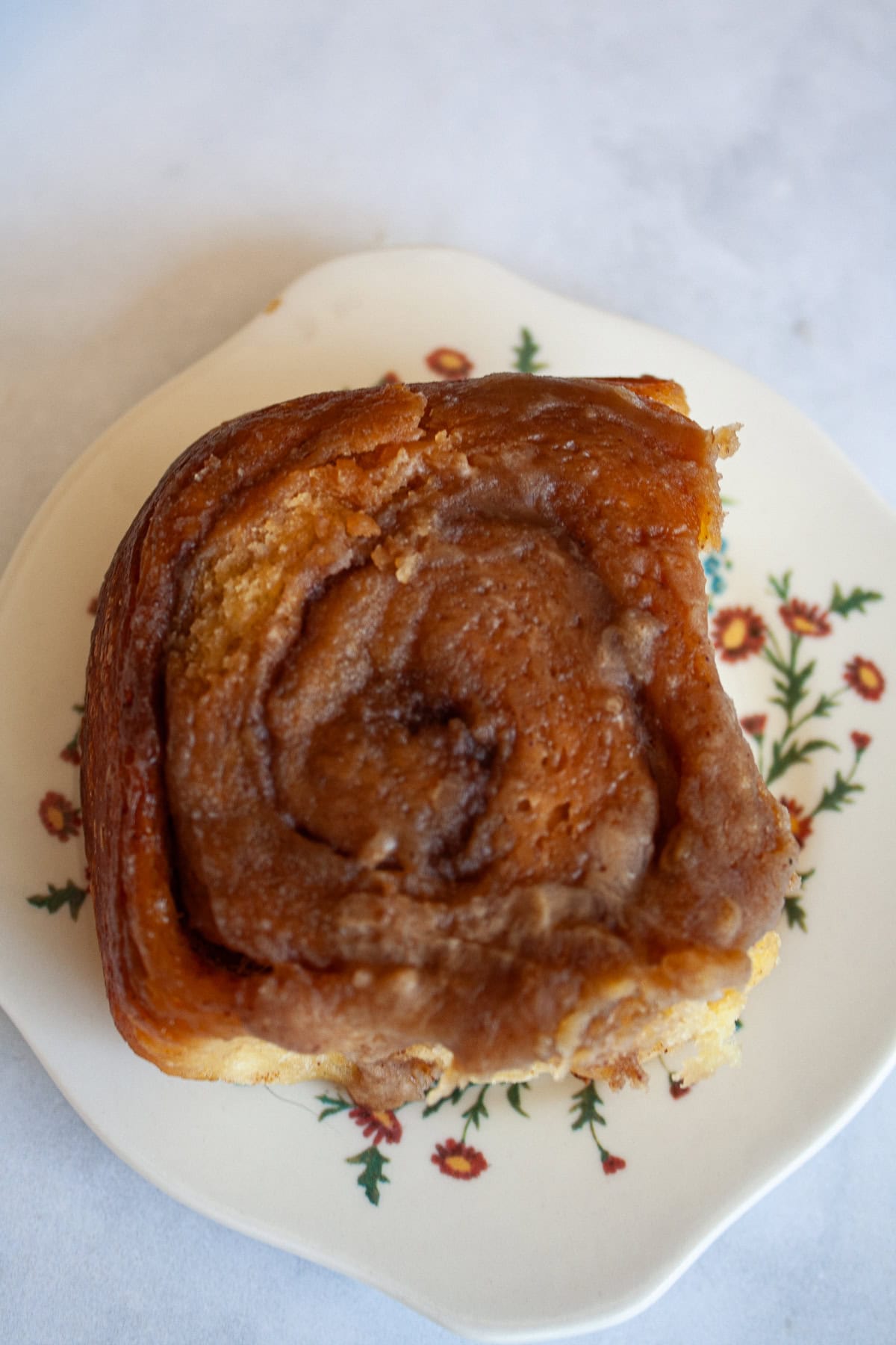 My homemade sticky buns recipe is make-ahead friendly and amazingly good! A thick maple syrup topping turns these into a bakery-worthy treat. Maple glaze tops a sticky bun on a plate.