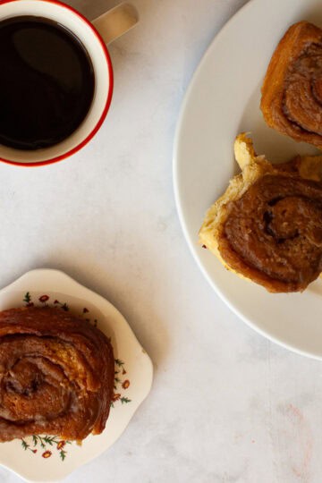 A cup of coffee next to plates of sticky buns.