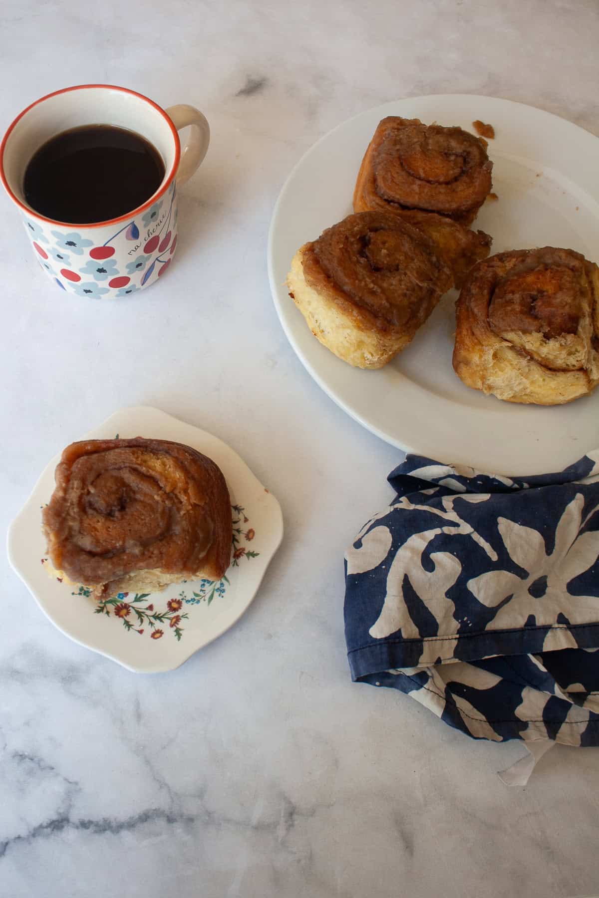 A plate of sticky buns, one on a plate, and a cup of coffee.