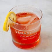 A glass of strawberry gin and tonic garnished with lemon.