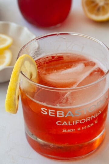 Lemons, strawberry syrup in the background and a glass of strawberry gin and tonic in the front.