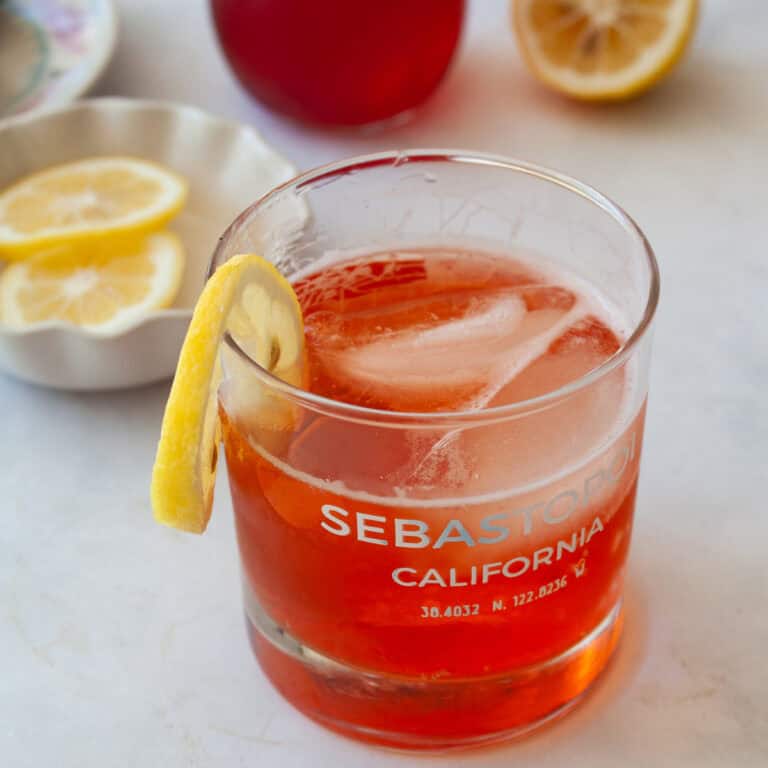 Lemons, strawberry syrup in the background and a glass of strawberry gin and tonic in the front.