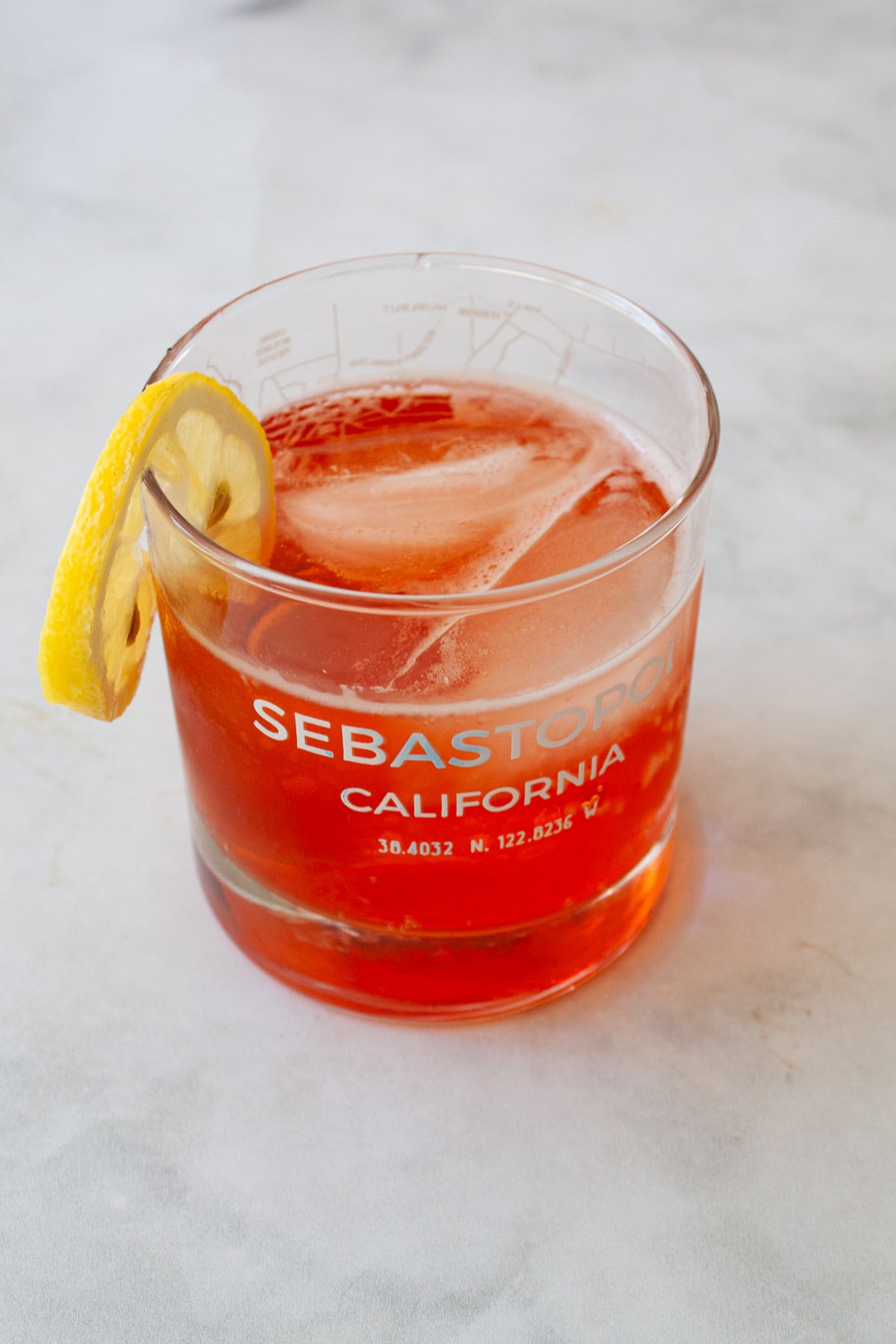 A glass of strawberry gin and tonic garnished with lemon.