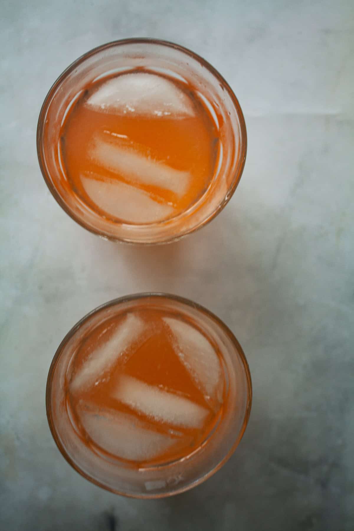 Sweet strawberry simple syrup is stirred into fresh lemon juice for a sweet-tart pitcher of homemade strawberry lemonade. Two glasses of homemade strawberry lemonade with ice.