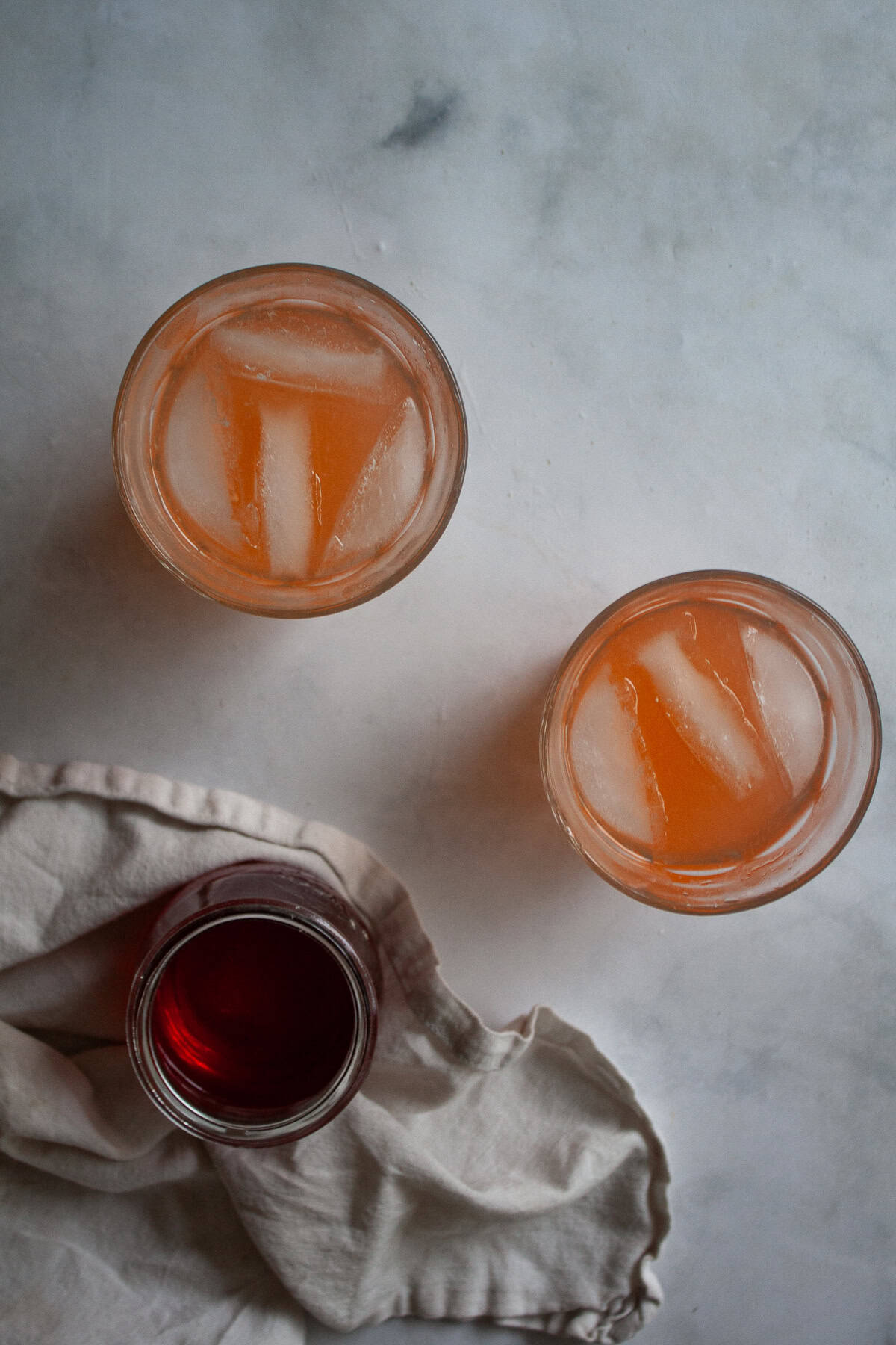 Sweet strawberry simple syrup is stirred into fresh lemon juice for a sweet-tart pitcher of homemade strawberry lemonade. Glasses of homemade strawberry lemonade next to a jar of strawberry simple syrup.
