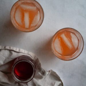 Glasses of homemade strawberry lemonade next to a jar of strawberry simple syrup.