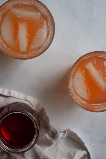 Glasses of homemade strawberry lemonade next to a jar of strawberry simple syrup.