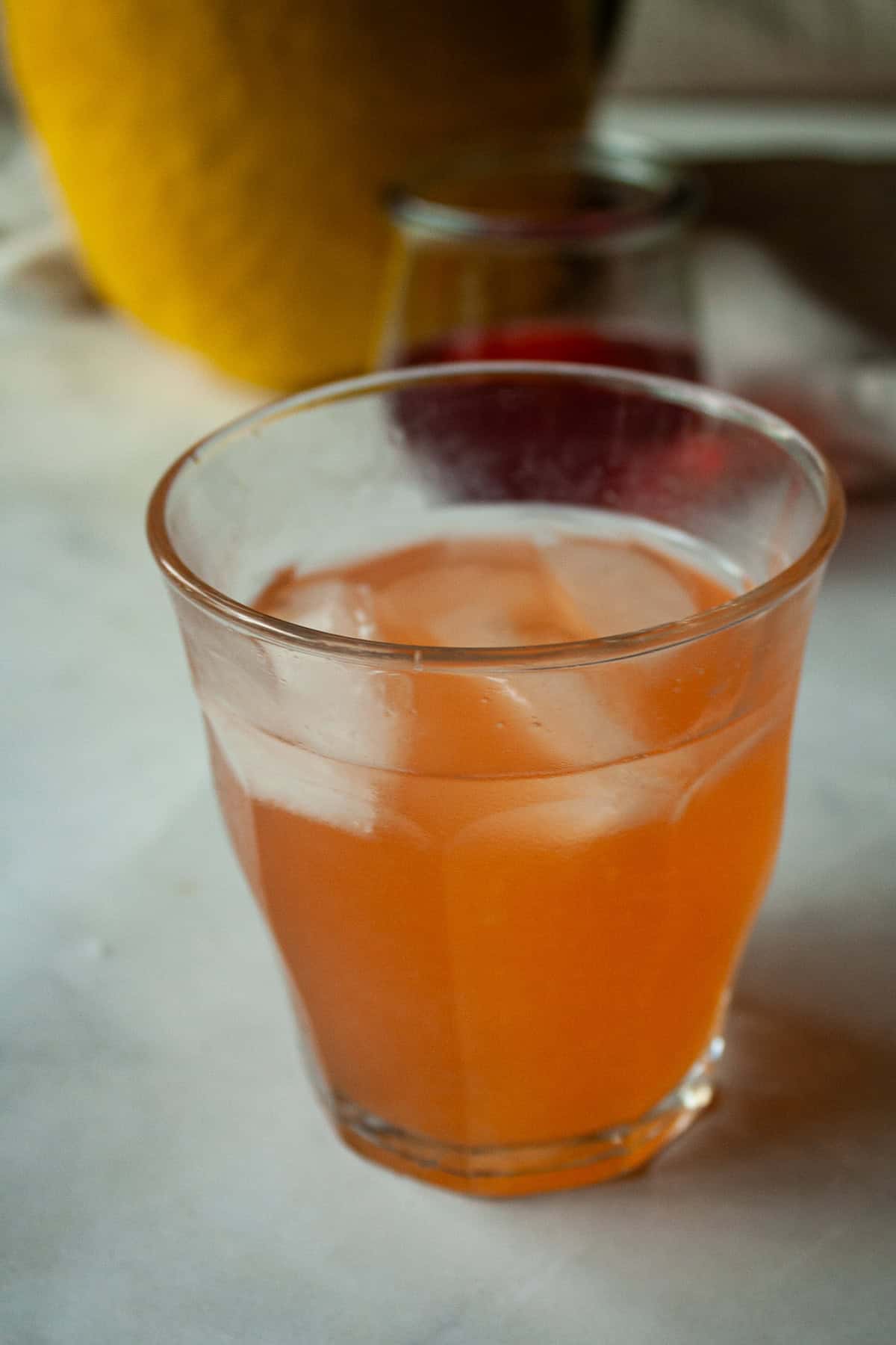 Sweet strawberry simple syrup is stirred into fresh lemon juice for a sweet-tart pitcher of homemade strawberry lemonade. A glass of homemade strawberry lemonade and a pitcher in the background.
