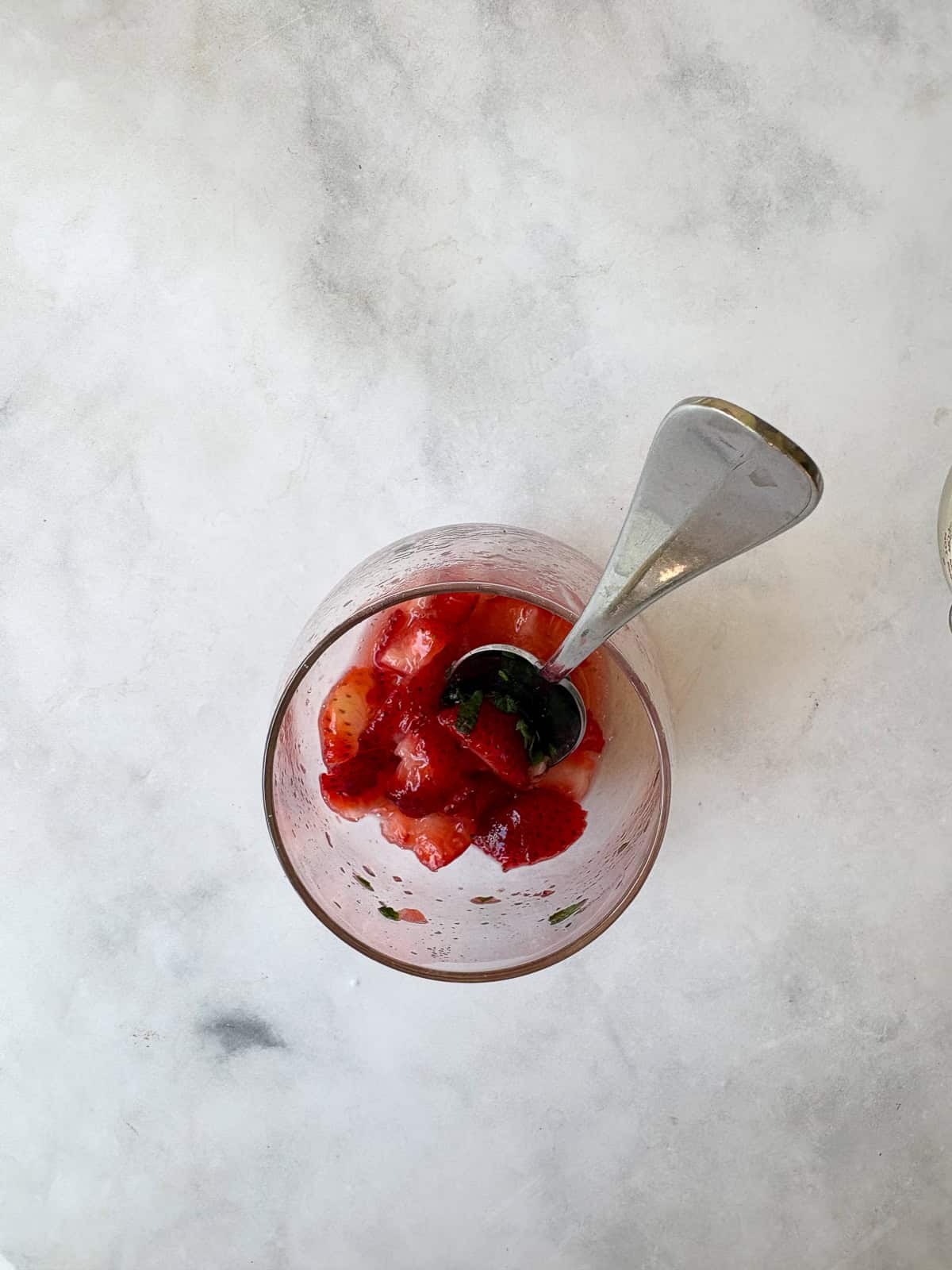 This strawberry mocktail is a not-too-sweet, non-alcoholic drink featuring juicy strawberries muddled with honey, lime, and mint. A spoon crushes strawberries in a glass for a strawberry mocktail.