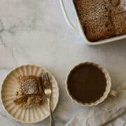 A pan of strawberry rhubarb cake, a coffee, and a slice on a plate.