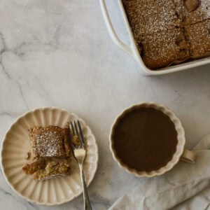 A pan of strawberry rhubarb cake, a coffee, and a slice on a plate.