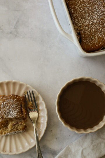 A pan of strawberry rhubarb cake, a coffee, and a slice on a plate.