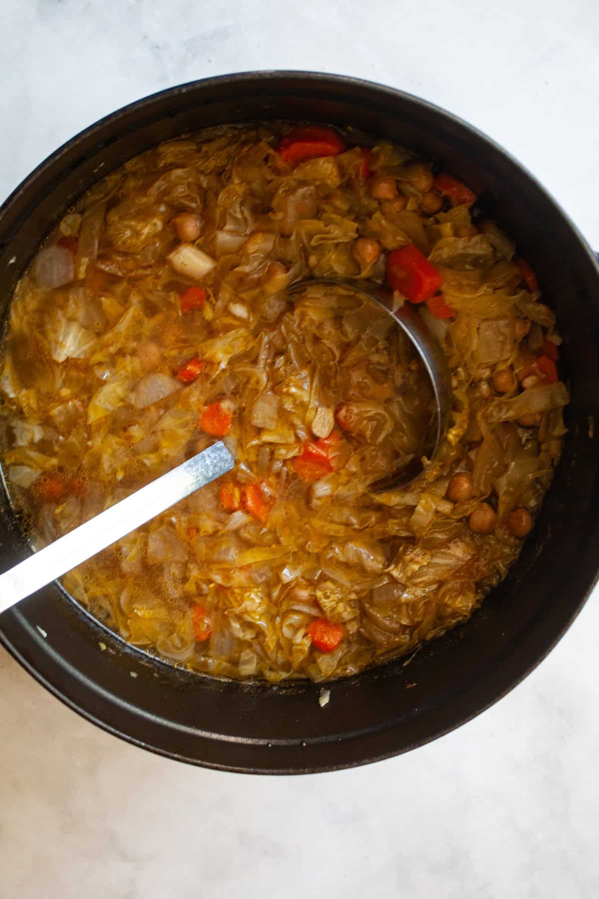 A brothy, satisfying vegetarian soup packed with tender cabbage, carrots, onions, garlic and plenty of chewy brown rice. A ladle rests in a pot of vegetarian cabbage soup.