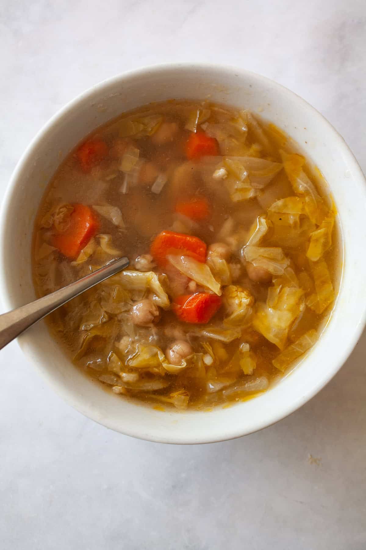 A brothy, satisfying vegetarian soup packed with tender cabbage, carrots, onions, garlic and plenty of chewy brown rice. A spoon dips into a bowl of vegetarian cabbage soup.